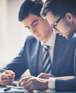 Image of two young businessmen using touchpad at meeting